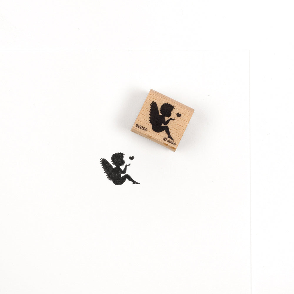 Ein Holzstempel und sein Abdruck, der die Silhouette eines Engels zeigt, der ein Herz bläst, mit detailreichen Motiven.