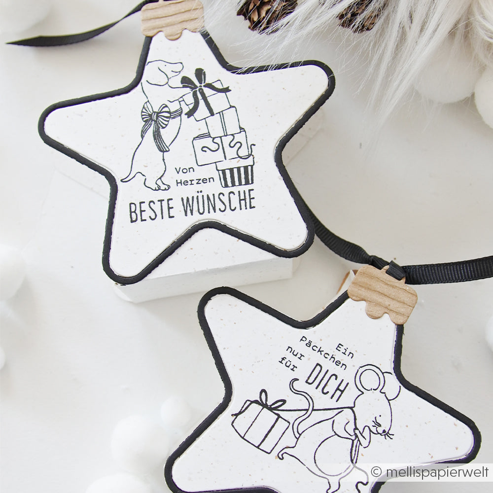Zwei sternförmige Beste Wünsche-Anhänger mit einem Hund und einer Maus, die Geschenke tragen.