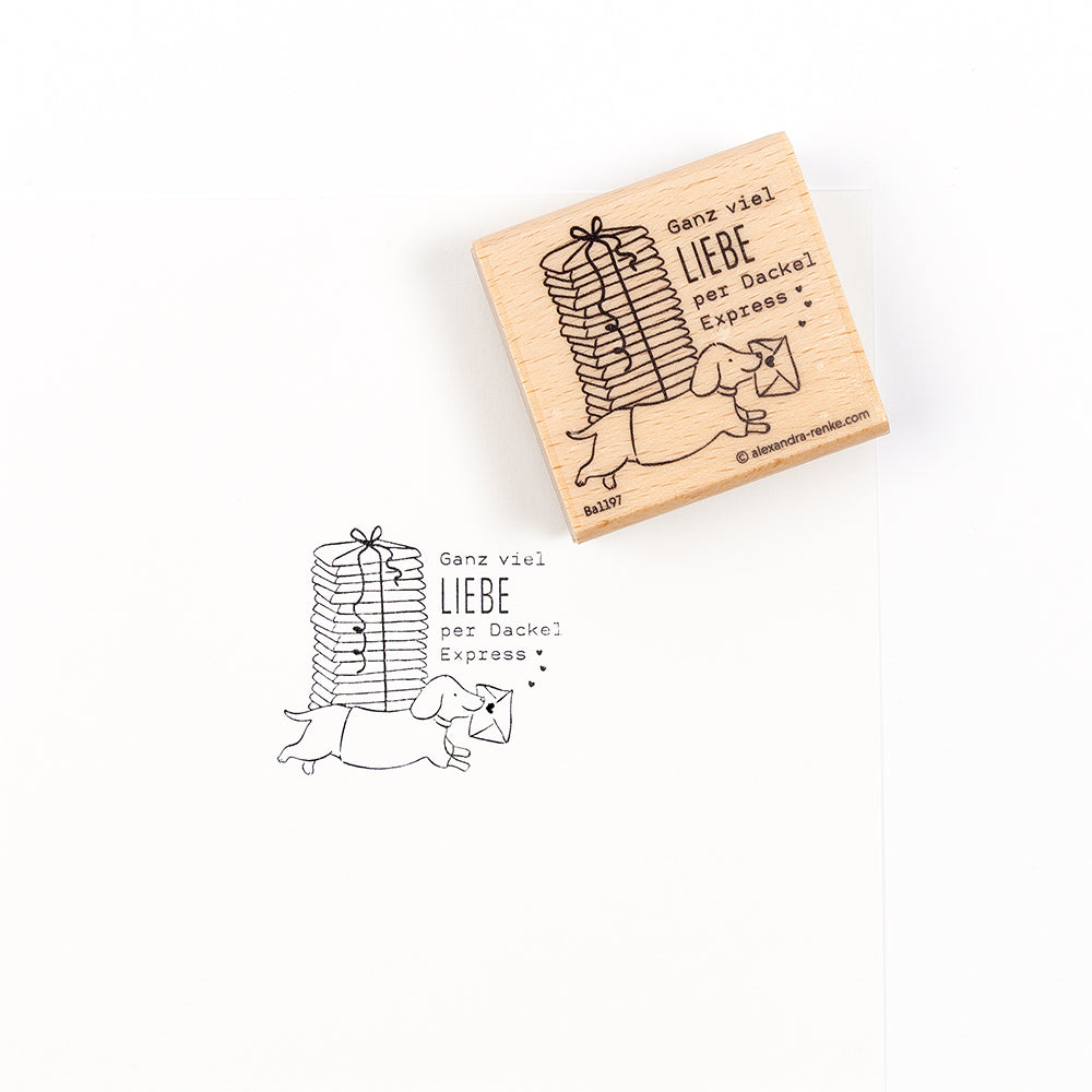 Ein Holzstempel und sein Abdruck, der einen Dackel zeigt, der einen Stapel Geschenke trägt, mit dem deutschen Text „Ganz viel LIEBE per Dackel-Express“ – eines von vielen Stempelmotiven.
