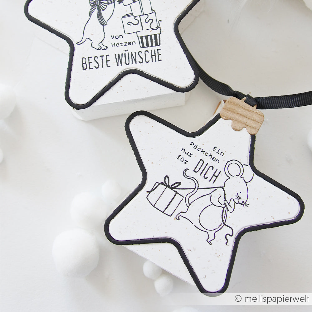 Zwei sternförmige Ornamente mit Holzstempel-Motiven von Mäusen, die Geschenke halten, sowie einem deutschen Text.