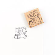Ein Holzstempel mit dem Stempelmotiv einer Maus, die ein Geschenk hält, und dem deutschen Text „Ein Päckchen nur für DICH“, ideal für Papierprojekte.