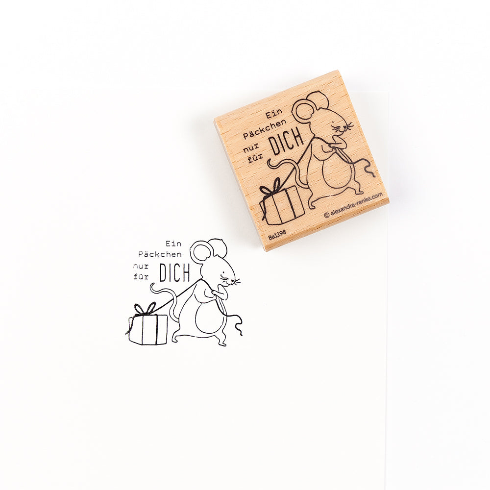 Ein Holzstempel mit dem Stempelmotiv einer Maus, die ein Geschenk hält, und dem deutschen Text „Ein Päckchen nur für DICH“, ideal für Papierprojekte.