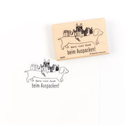 Ein Holzstempel mit dem Abdruck eines Dackels, der Geschenke trägt, und dem Text „Ganz viel Spaß beim Auspacken!“, ideal für Papierprojekte.