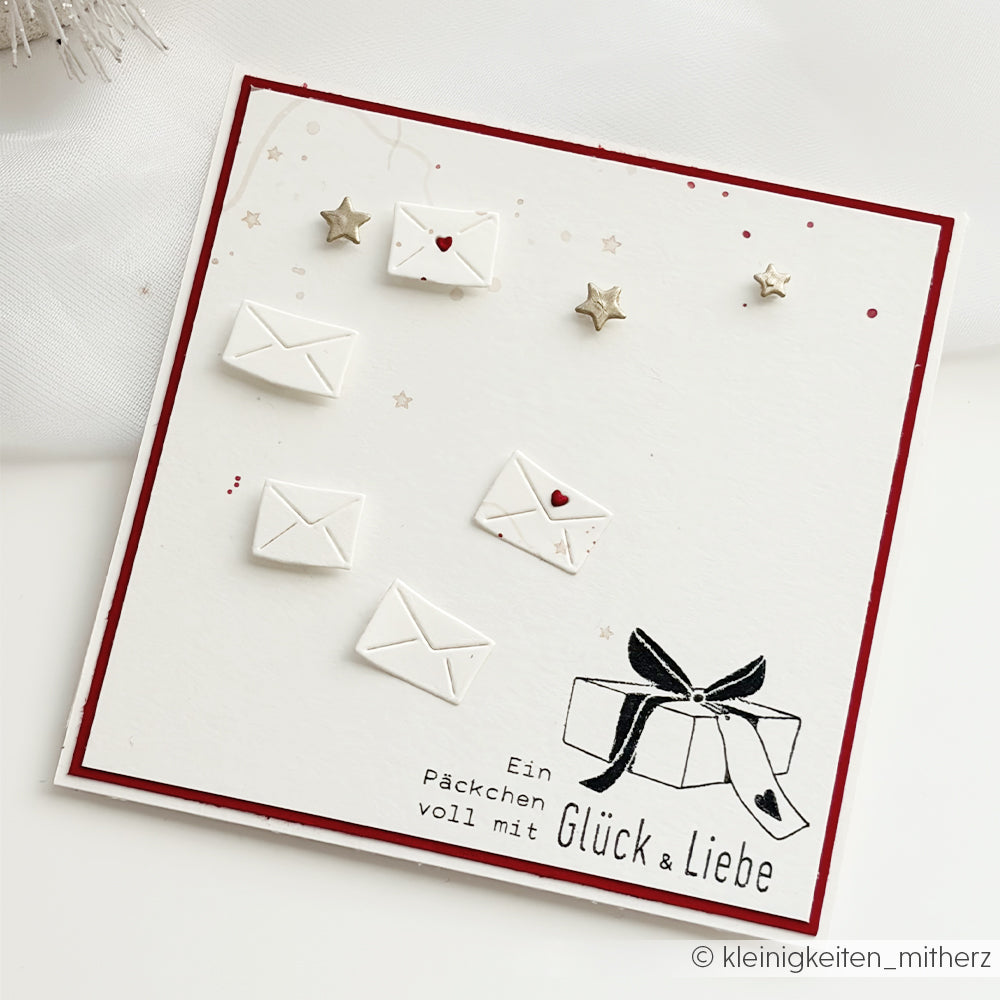 Handgefertigte Karte mit Papiermotiven, Sternverzierungen und der Aufschrift Ein Päckchen voll mit Glück & Liebe.