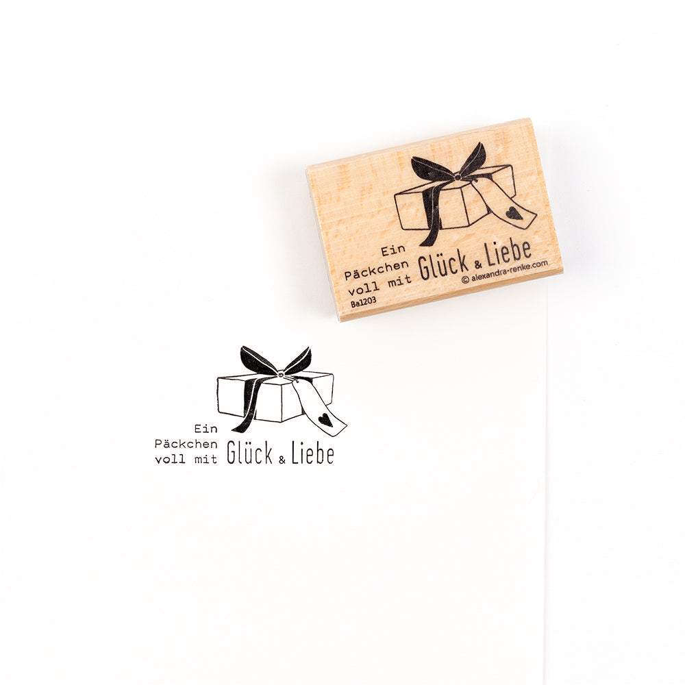 Ein Holzstempel mit Geschenkverpackungsmotiv und dem deutschen Text „Ein Päckchen voll mit Glück & Liebe“ – ideal, um Ihren Papierprojekten eine persönliche Note zu verleihen.