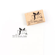 Ein Holzstempel mit Geschenkverpackungsmotiv und dem deutschen Text „Ein Päckchen voll mit Glück & Liebe“ – ideal, um Ihren Papierprojekten eine persönliche Note zu verleihen.