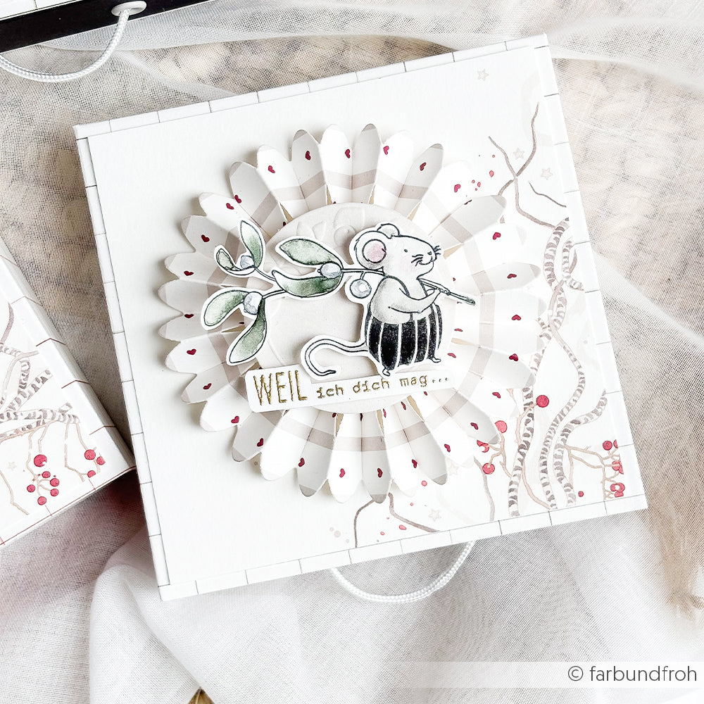 Handgefertigte weiße Geschenkbox mit einer Papierblumenrosette, auf der eine Maus mit Mistelzweig abgebildet ist, verziert mit einem Holzstempel und dem Schriftzug „WEIL ich dich mag“.