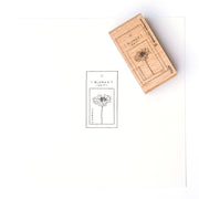 Ein Holzstempel von Alexandra Renke erzeugt einen Blumenabdruck mit schwarzer Tinte auf einem BLUMEN ZEIT-Anhänger, der mit einem Stempelkissen hergestellt wurde.