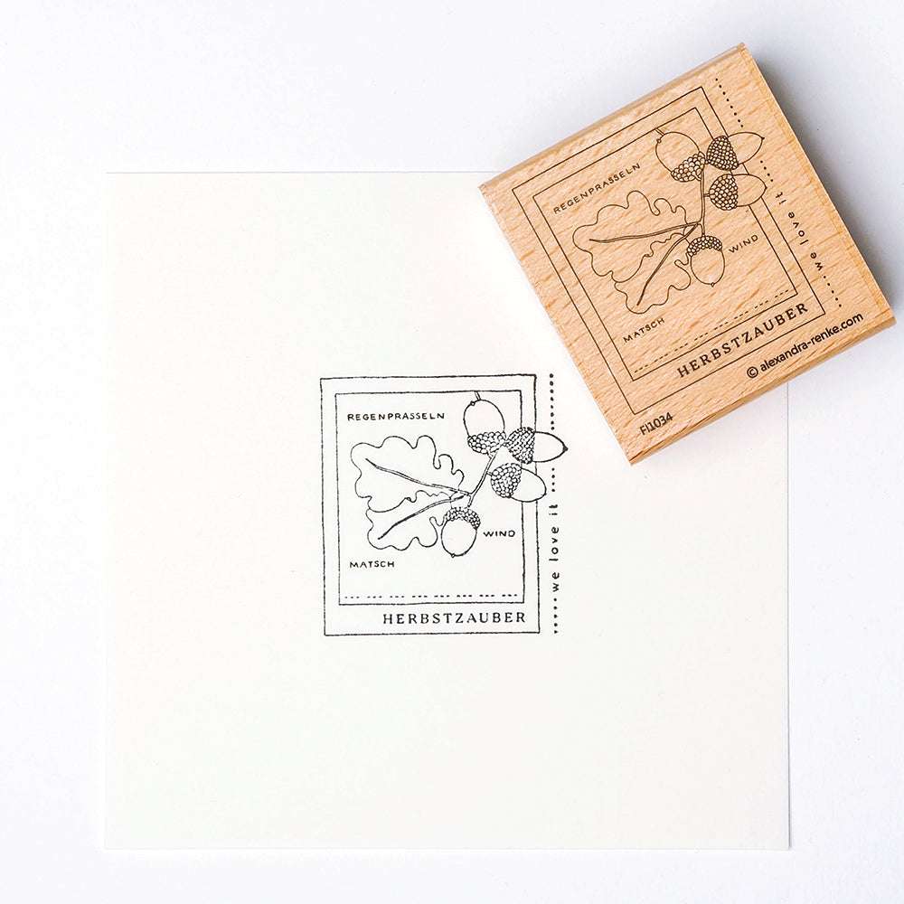 Mit dem Holzstempel von Alexandra Renke entstehen herbstliche Abdrücke mit Eicheln, einem Eichenblatt und Wörtern wie "Eicheln Herbstzauber" - ideale Stempelmotive für saisonale Bastelarbeiten auf Papier.