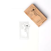 Ein rechteckiger Holzstempel von Alexandra Renke mit einer Mohnblume als Motiv liegt neben seinem frisch gedruckten Abdruck auf weißem Papier.