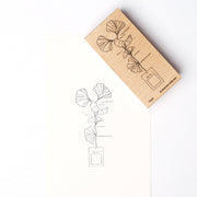 Ein hölzerner Alexandra Renke Holzstempel und sein Aufdruck - eine einfache Strichzeichnung eines goldenen Gingko-Blattes und ein Rechteck auf weißem Papier - sind bereit, mit Ihrem Lieblingsstempelkissen kombiniert zu werden.