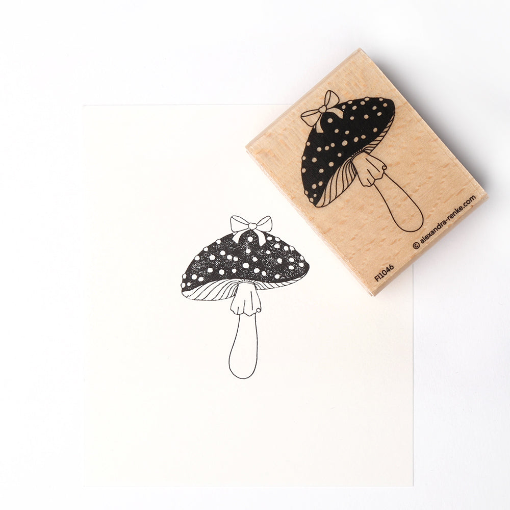 Der Alexandra Renke Fliegenpilz Stempel und der dazugehörige Abdruck zeigen einen Pilz mit gepunktetem Hut und einer kleinen Schleife auf der Spitze.