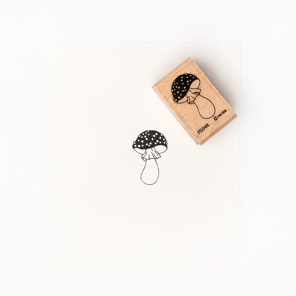 Ein Holzpilzstempel von Alexandra Renke ruht neben seinem gestempelten Bild auf weißem Papier und ist damit ideal für kreative Papierprojekte.