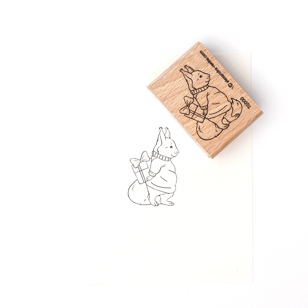 Ein Holzstempel von Alexandra Renke und Papier zeigen ein Kaninchen in einem Pullover, das eine Tasche über der Schulter trägt.