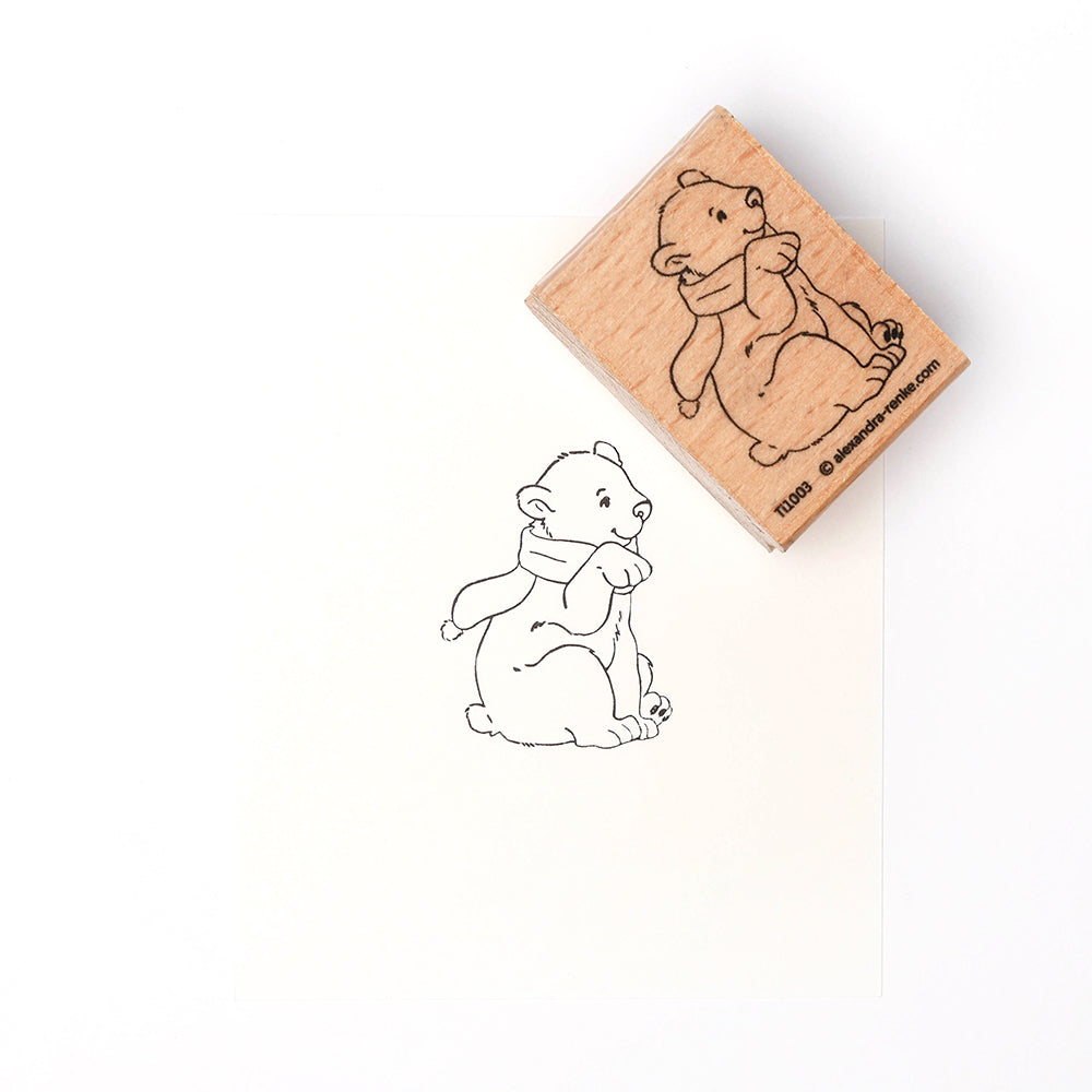 Ein Holzstempel von Alexandra Renke mit einem Druck eines sitzenden Bären mit Schal, inspiriert von Eisbärbaby Flocke, auf weißem Hintergrund.
