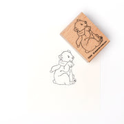 Ein Holzstempel von Alexandra Renke mit einem Druck eines sitzenden Bären mit Schal, inspiriert von Eisbärbaby Flocke, auf weißem Hintergrund.
