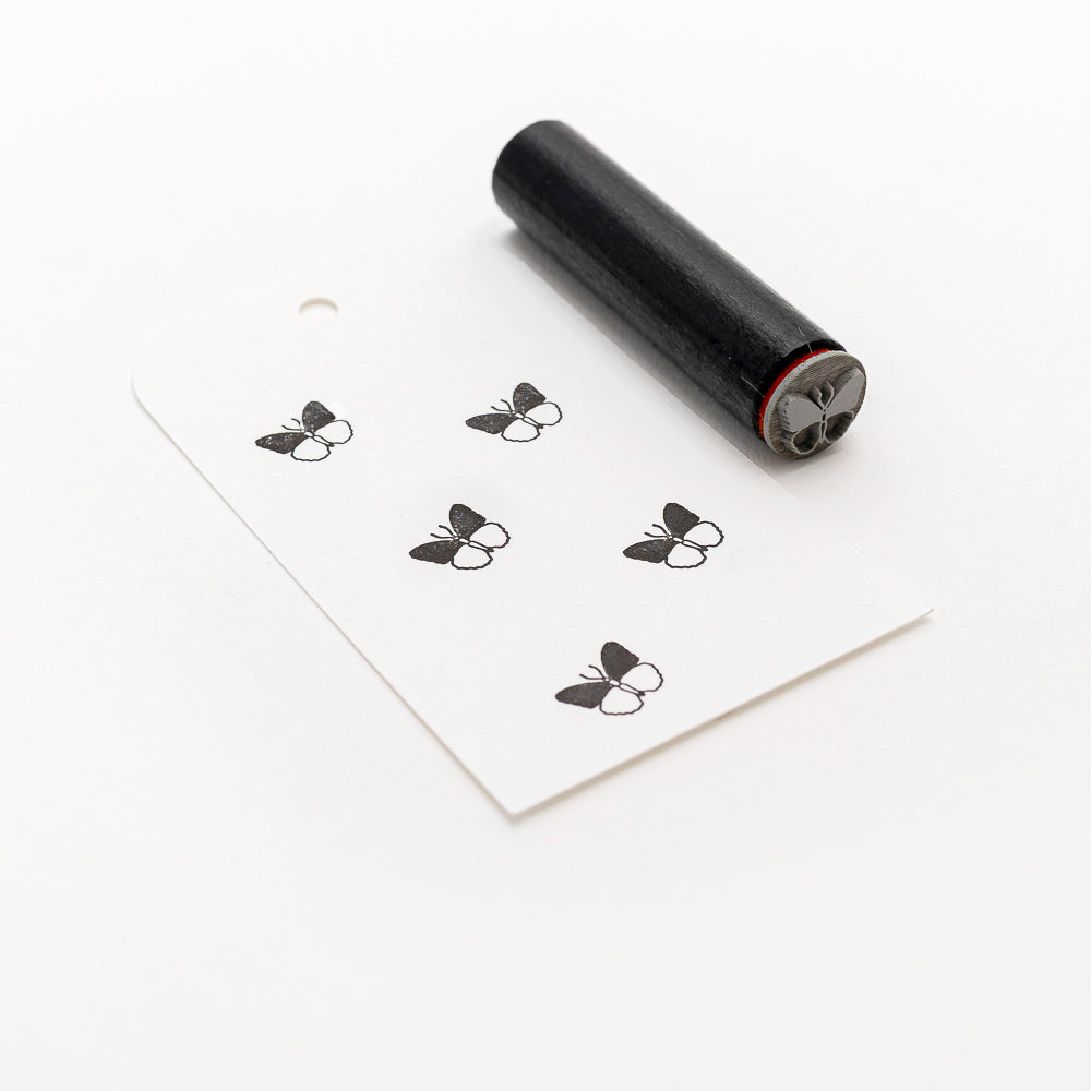 Schwarzer Gummistempel und gestempelter Schmetterling auf einem weißen Anhänger mit Loch, mit dem Alexandra Renke Mini Schmetterling Holzstempel als elegantem Akzentstempel.