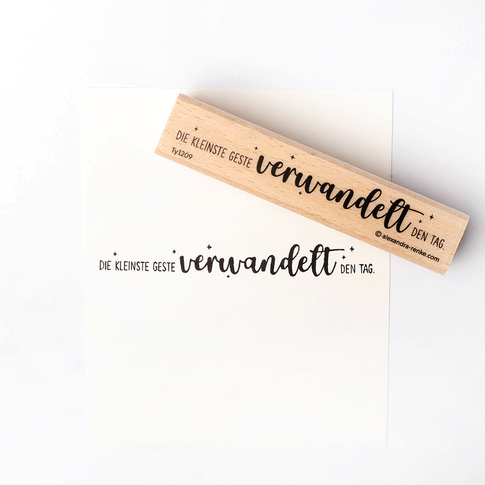 Ein hölzerner Alexandra Renke Holzstempel und Papier mit deutschem Text: Die kleinste Geste verwandelt den Tag-ideal für Papierprojekte und kreative Momente.