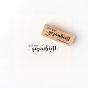 Ein Holzstempel von Alexandra Renke stempelt in schwarzer Tinte "HEUTE WIRD gezaubert!" - ein charmantes Detail für Ihre Papierprojekte.