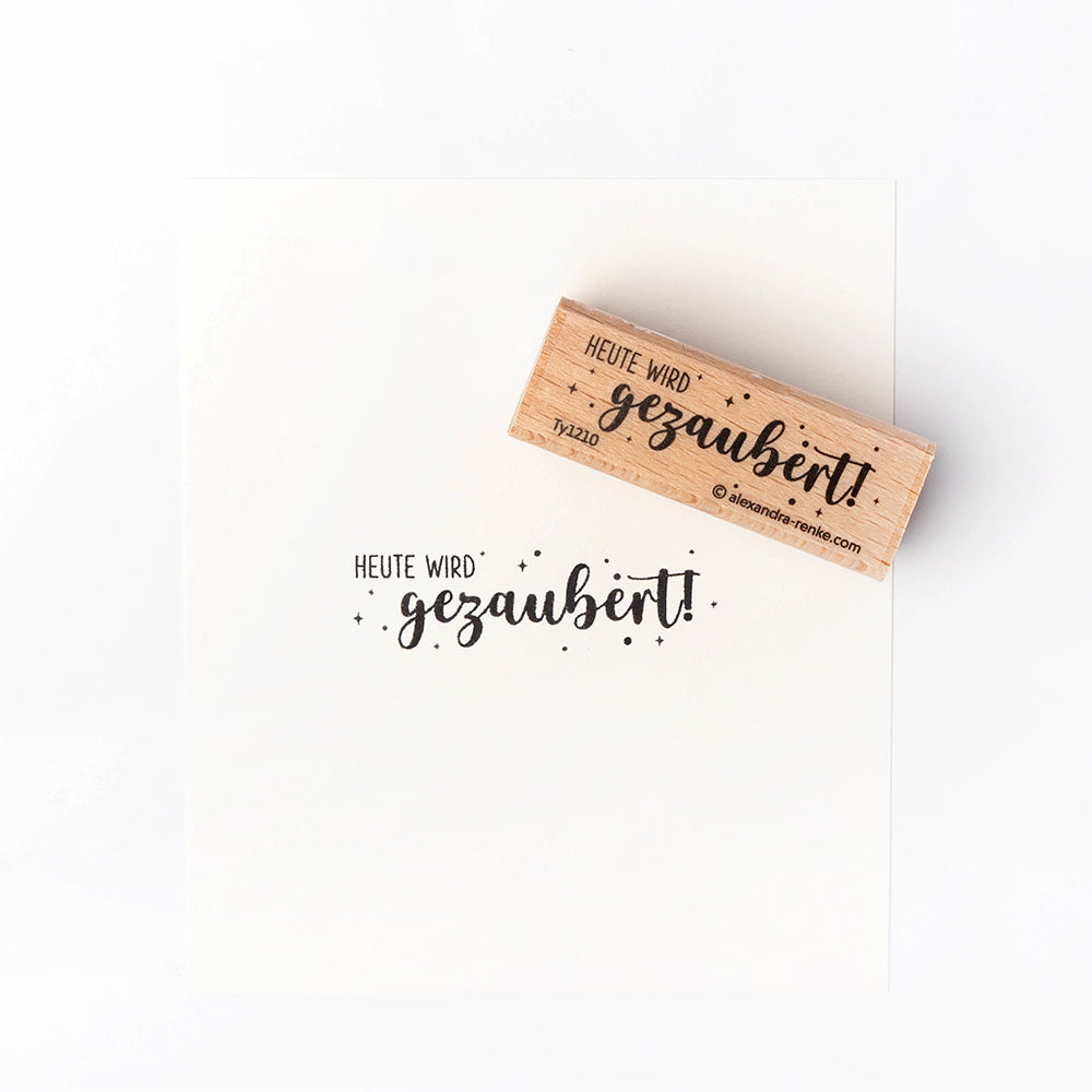 Ein Holzstempel von Alexandra Renke stempelt in schwarzer Tinte "HEUTE WIRD gezaubert!" - ein charmantes Detail für Ihre Papierprojekte.