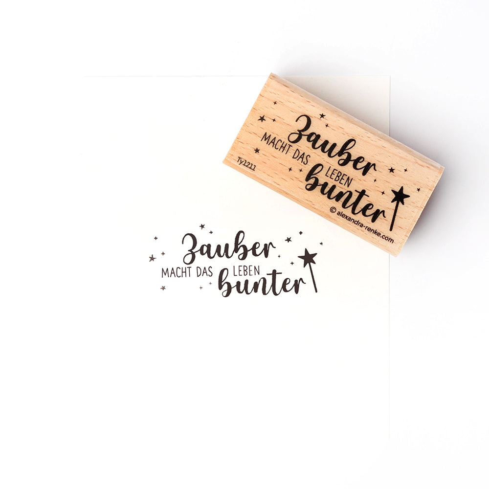 Ein Alexandra Renke Holzstempel mit Stempelgummi und dem deutschen Text "Zauber macht das Leben bunter" sowie einem Zauberstab-Motiv, ideal für Papierprojekte und bestens für weißen Karton geeignet.