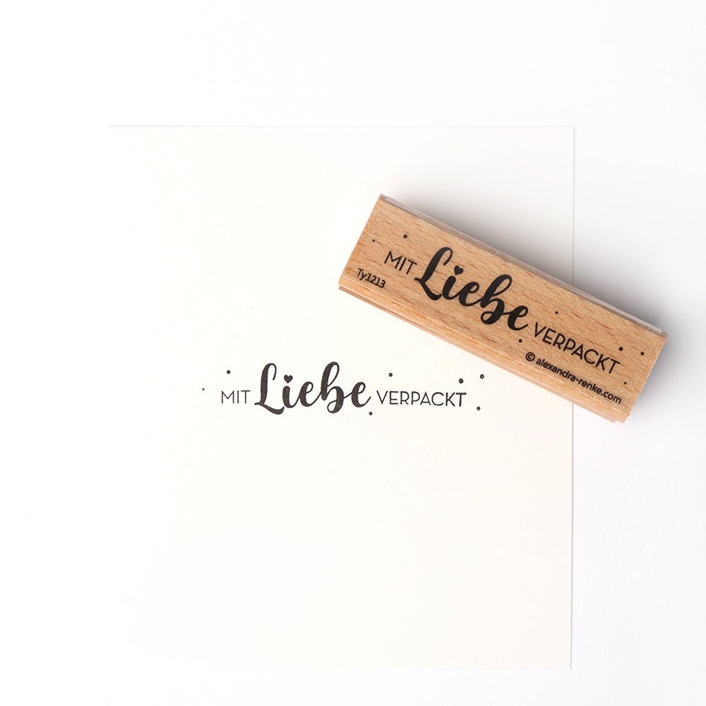 Die Alexandra Renke Holzstempel und Stempelkissen stempeln "Mit Liebe verpackt" in deutscher Sprache auf Papier.