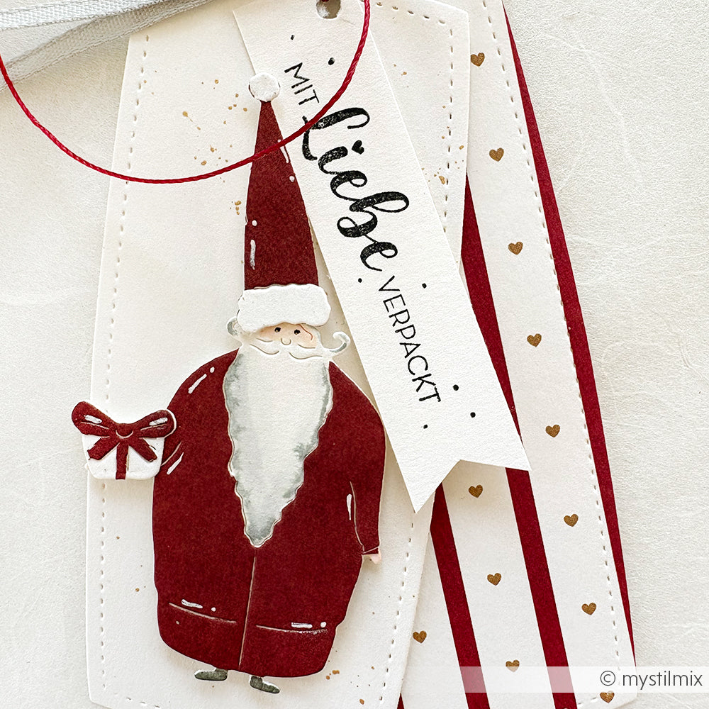 Alexandra Renke Geschenkanhänger mit rotem Weihnachtsmann, kleinem Geschenk, Herzmustern und dem Spruch "Mit Liebe verpackt", gestempelt mit Stempelkissen und Holzstempel.
