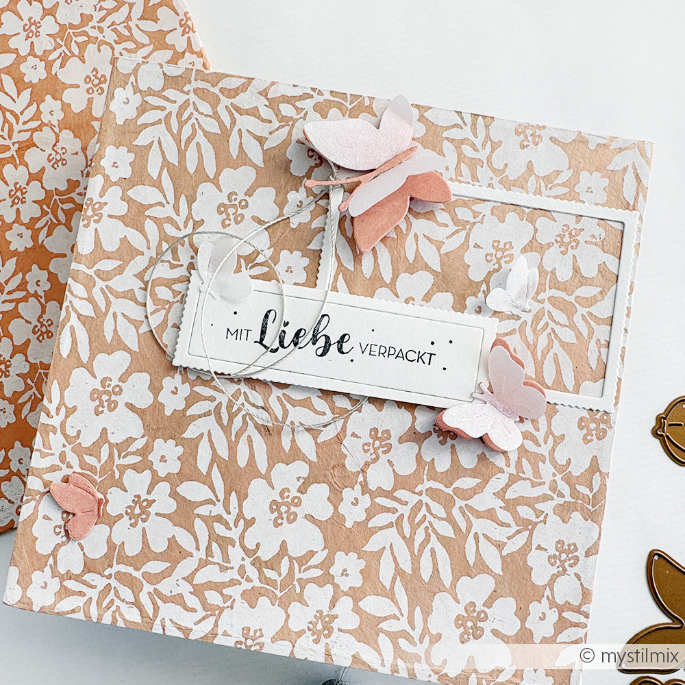 Floral gemusterte Geschenkbox mit rosa Schmetterlingen und einem Holzstempel mit der Aufschrift "Mit Liebe verpackt" - perfekt für Stempel für Papierprojekte von Alexandra Renke.