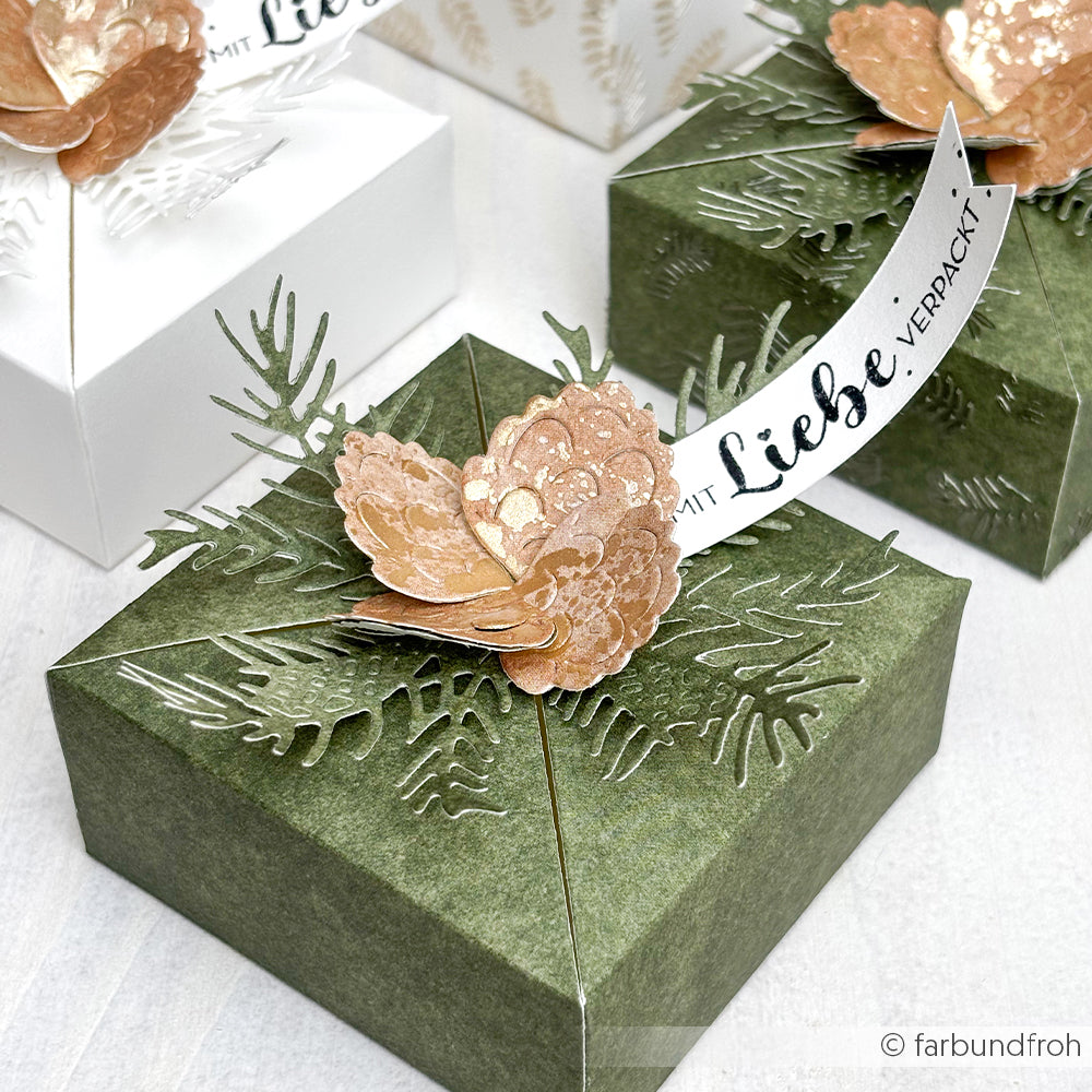 Eine grüne Geschenkbox von Alexandra Renke, verziert mit Tannennadeln aus Papier, einer Blume und einem charmanten Holzstempel-Banner mit der Aufschrift "Mit Liebe verpackt.