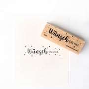 Ein hölzerner Motivstempel von Alexandra Renke und gestempeltes Papier tragen beide die Aufschrift "Wünsch, dir was" mit Sternendekor auf Weiß - ein ideales Stempelprojekt für Anfänger.