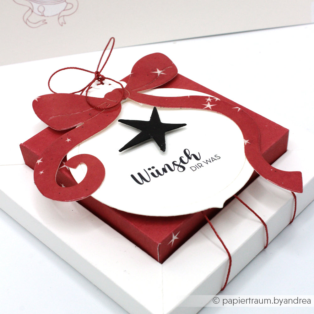Die rote Geschenkbox von Alexandra Renke ist mit einer großen Schleife, einem Sternendekor und dem Schriftzug "Wünsch dir was" auf einem weißen Anhänger versehen - ideal für Papierprojekte oder in Kombination mit Holzstempeln und Stempelkissen, um einzigartige, kreative Geschenke zu gestalten.