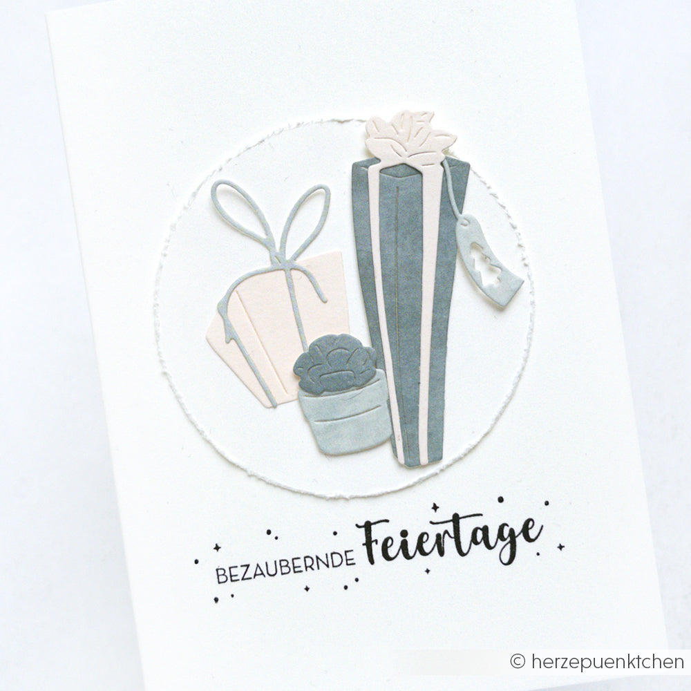 Drei pastellfarbene Geschenkschachteln mit Schleifen und einer weißen Karte mit einem deutschen Weihnachtsgruß, verziert mit hochwertigen Stempeln von Alexandra Renke für eine elegante Note.