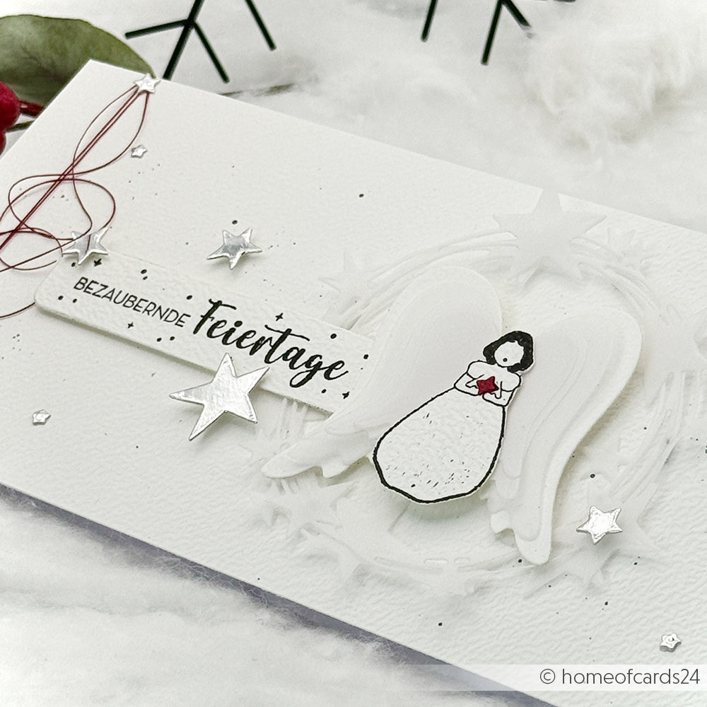 Handgefertigte Weihnachtskarte von Alexandra Renke mit einem Engel, silbernen Sternen, rotem Faden und "Bezaubernde Feiertage" in Deutsch. Gefertigt mit hochwertigem Holz und einzigartigen Holzstempeln für elegante, detaillierte Designs.