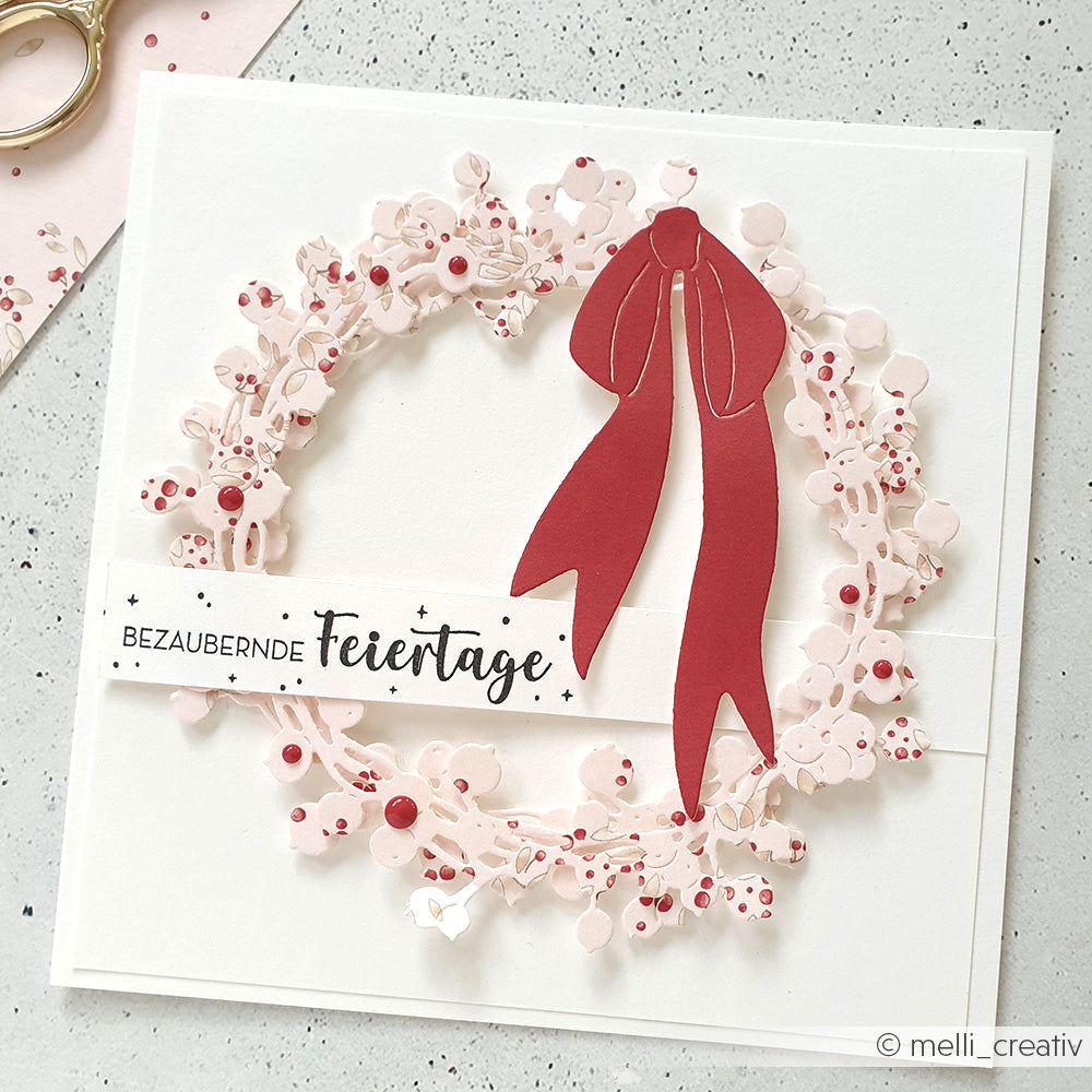 Handgefertigte Weihnachtskarte von Alexandra Renke mit rosa Kranz, roter Schleife und deutschem Text "Bezaubernde Feiertage", mit detailreichen Motiven und hochwertigen Holzstempeln für eine einzigartige festliche Note.
