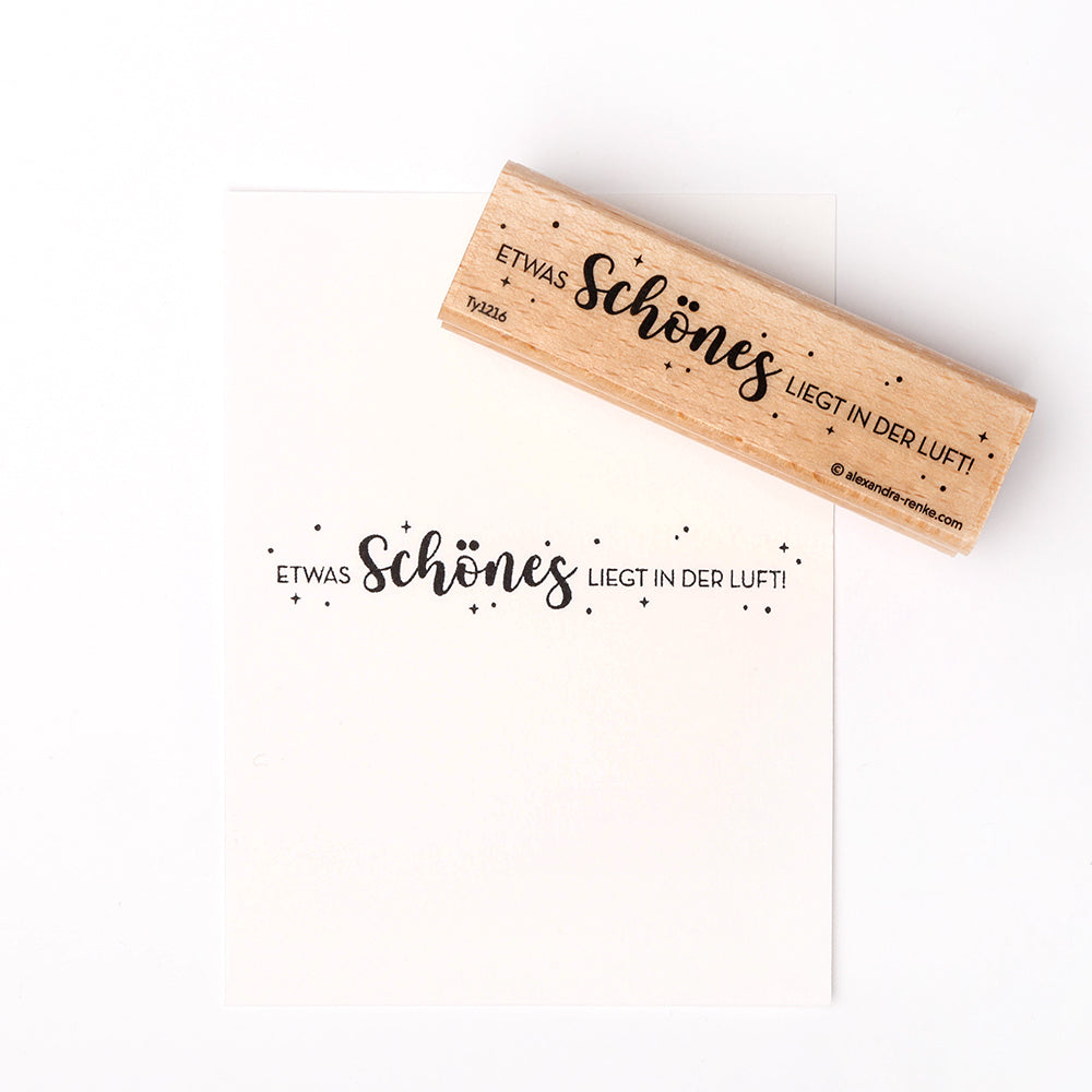 Der Alexandra Renke Holzstempel mit Papier zeigt "Etwas Schönes liegt in der Luft!" und dekorative Sterne - ideal als Inspiration für Ihre Papierprojekte.