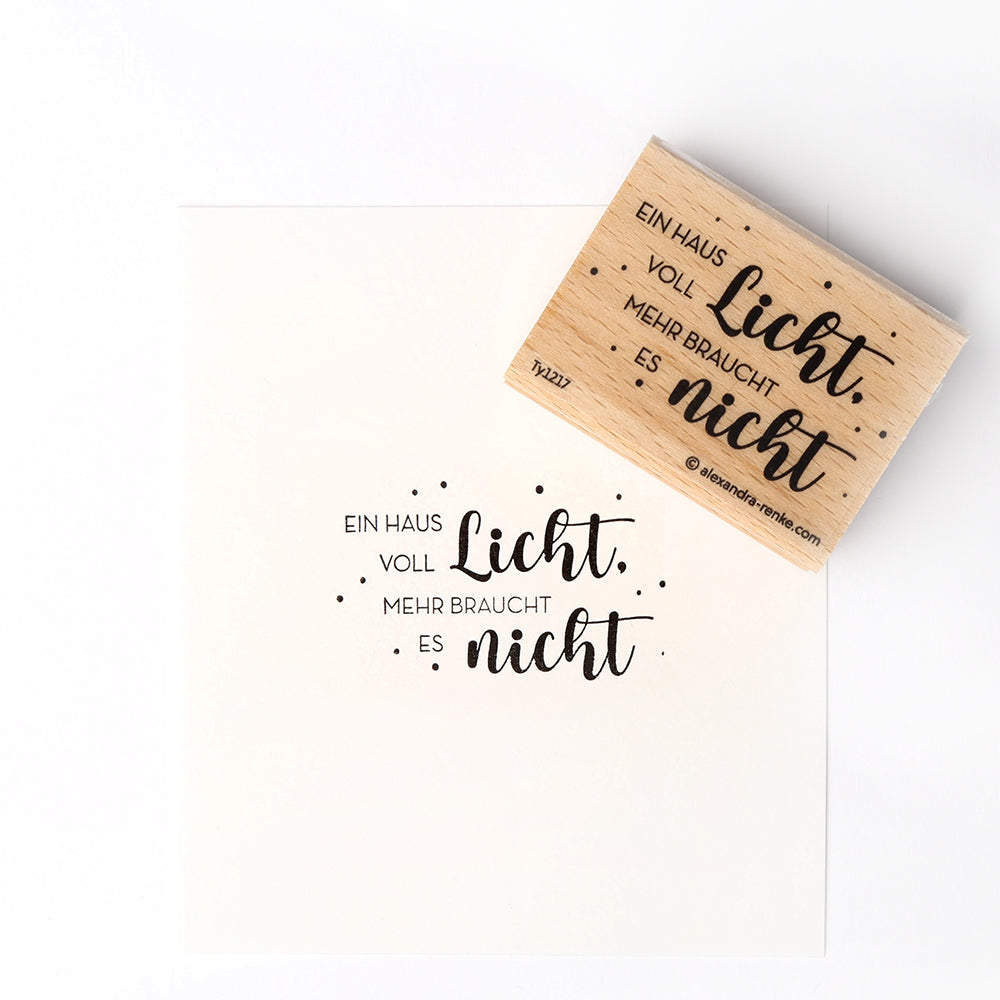 Ein Holzstempel von Alexandra Renke und sein Abdruck mit dem Text "Ein Haus voll Licht. Mehr braucht es nicht." - perfekt für kreative Papierprojekte.