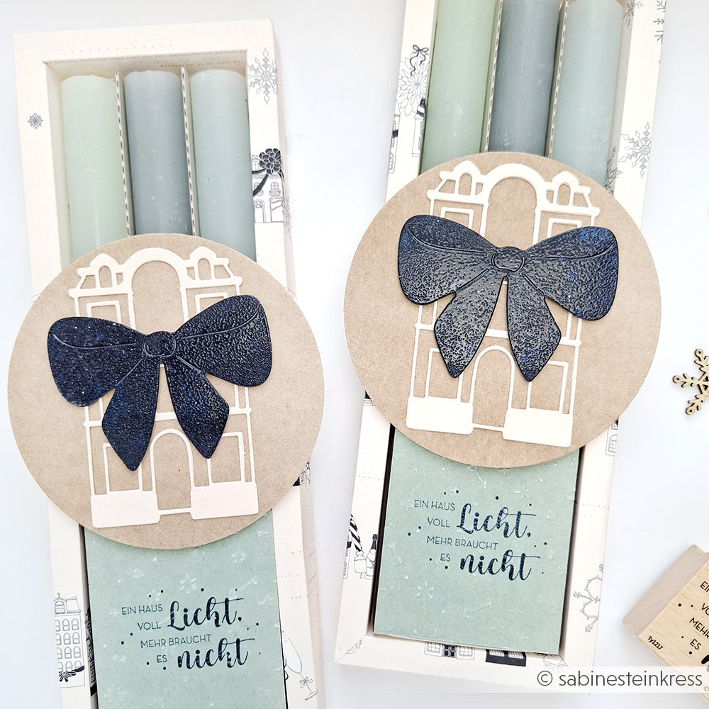 Zwei Sets mit pastellfarbenen Kerzen von Alexandra Renke in dekorativen Schachteln mit Schleifen und Hausmotiven, die jeweils mit einem deutschen Zitat versehen sind - wunderschön gepaart mit einem hochwertigen Holzstempel oder Stempelgummi für ein charmantes Geschenkset.