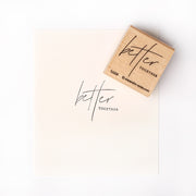Ein Alexandra Renke Holzstempel und Papier mit dem handgeschriebenen Satz "better together" in schwarzer Tinte auf weißem Hintergrund.