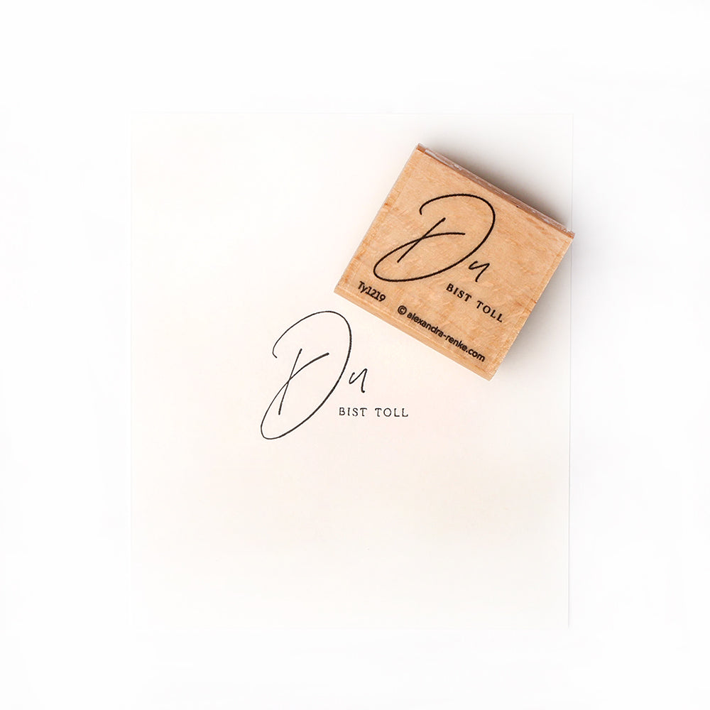 Holzstempel von Alexandra Renke und gestempeltes Papier mit "Du bist toll" in schwarzer Schreibschrift - ideal für Ihre Papierprojekte oder individuelle Stempelgummi-Designs.