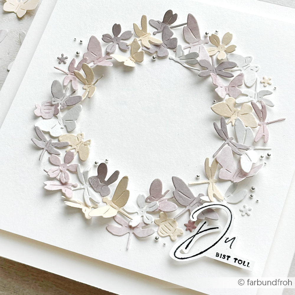 Ein zarter Papierkranz aus pastellfarbenen Blüten und Blättern schmückt eine weiße Karte von Alexandra Renke, die mit dem Holzstempel "Du bist toll" bestempelt ist.