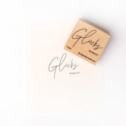 Der hochwertige Holzstempel von Alexandra Renke mit handschriftlichem "Glücks Moment" auf weißem Hintergrund ist ein schönes Stempelmotiv für besondere Anlässe.