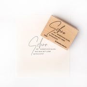 Ein Holzstempel von Alexandra Renke und gestempeltes Papier mit deutschem Text in eleganter Schrift auf weißem Hintergrund.