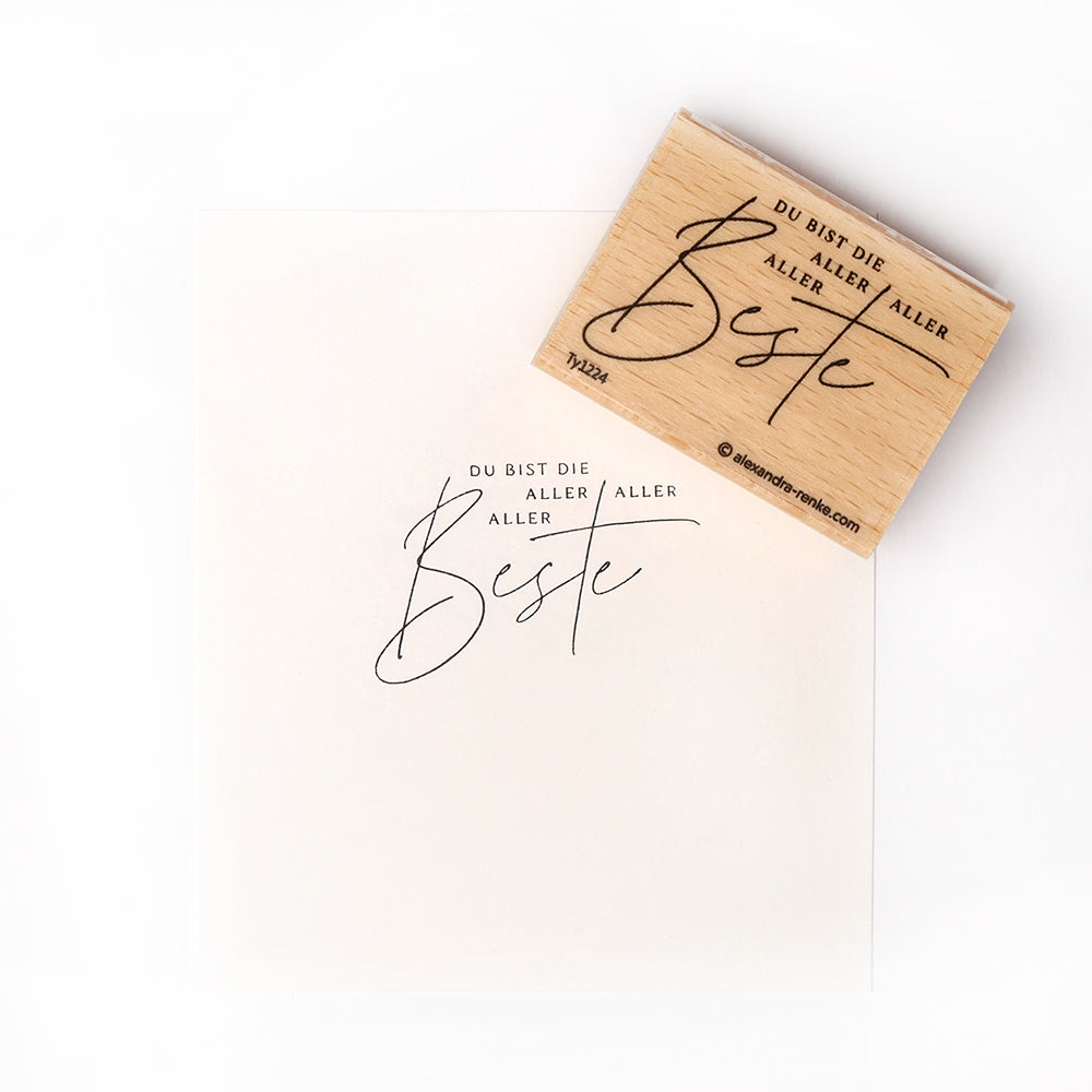 Ein Alexandra Renke Holzstempel druckt "DU BIST DIE ALLERALLERER BESTEN" in Schreibschrift auf weißes Papier - ideal für kreative Papierprojekte und Stempelgummi-Gestaltungen.