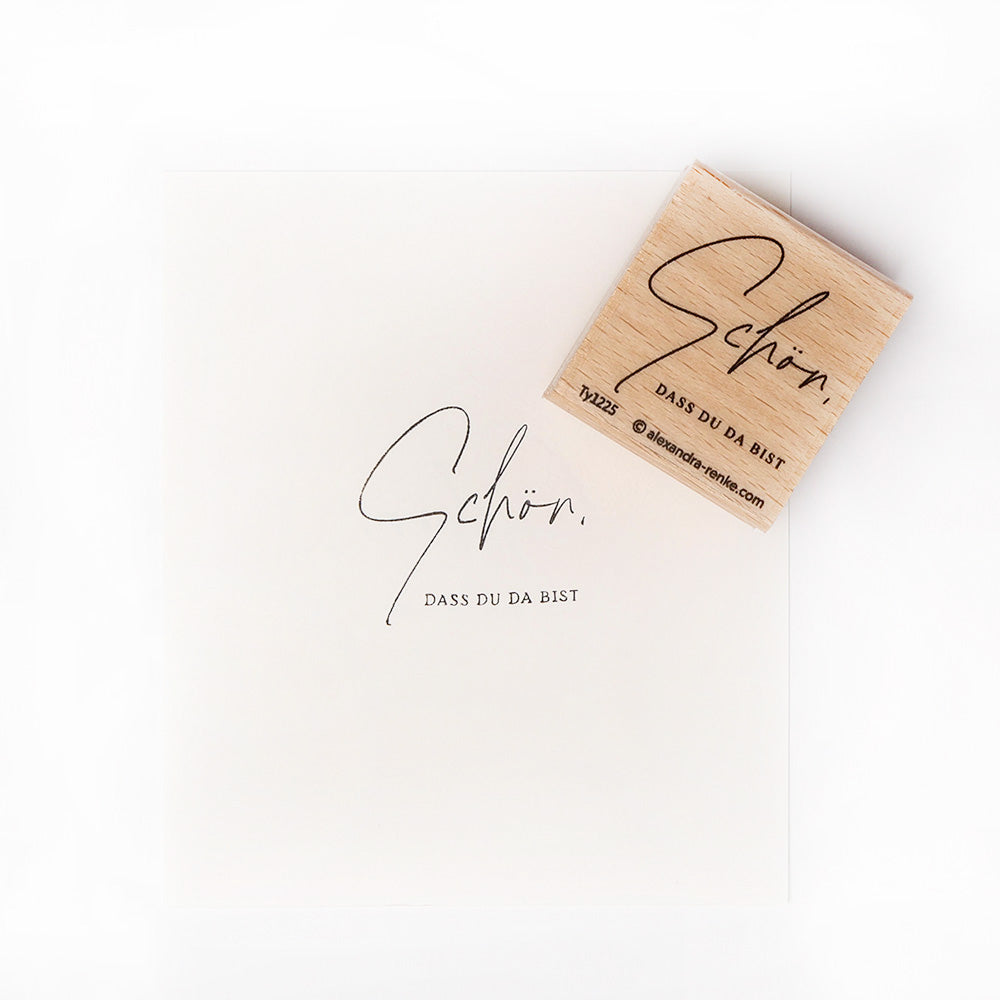 Auf dem Holzstempel und dem Papier von Alexandra Renke steht "Schön, dass du da bist" in Schreibschrift - ideal zum Kombinieren mit Ihren Lieblings-Stempelkissen oder Stempelgummi.