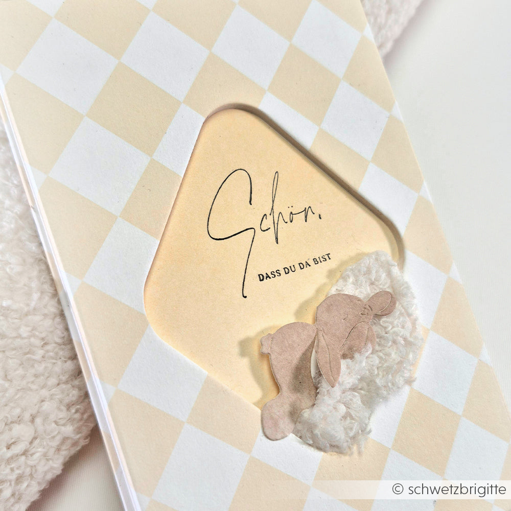 Eine Karte von Alexandra Renke mit einem Hasen und dem Spruch "Schön, dass du da bist" auf einem beige-karierten Hintergrund - ideal für Papierprojekte oder zur Verwendung mit Ihrem Lieblingsholzstempel.