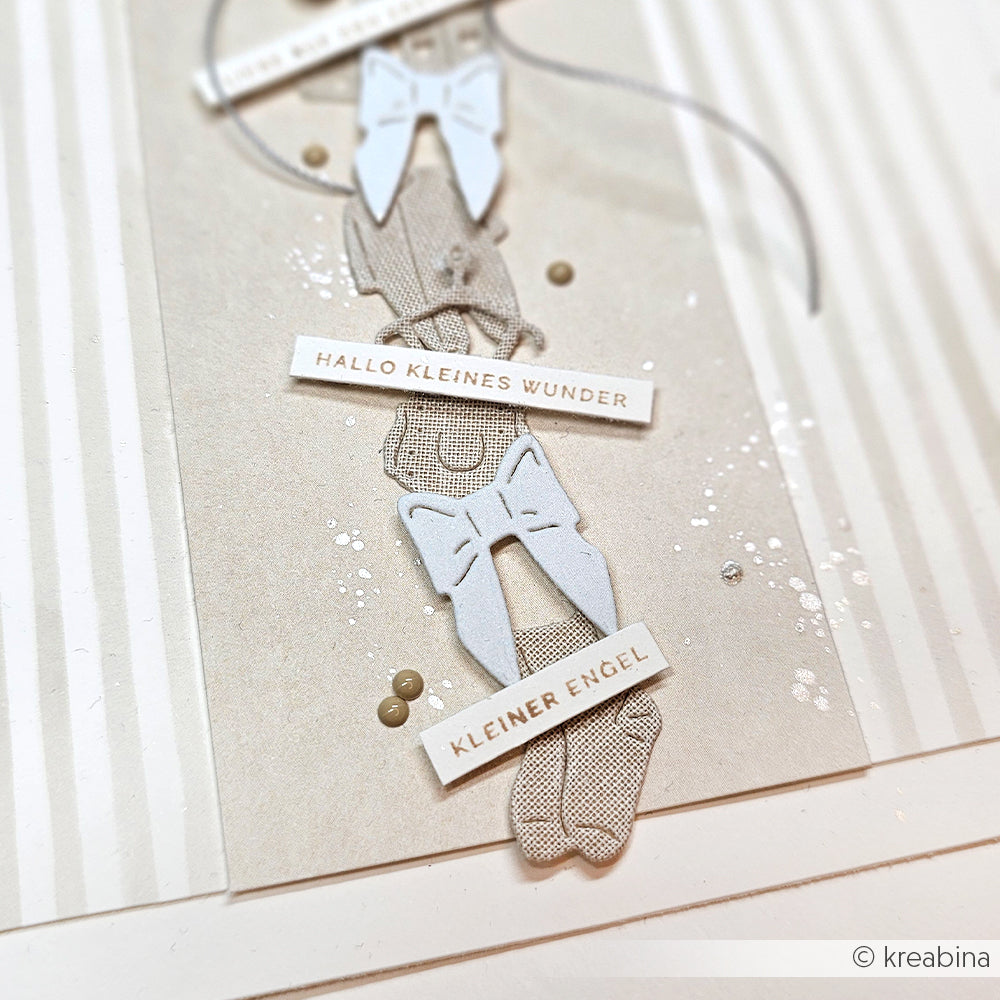 Neutral getönte Karte von Alexandra Renke mit Schleifen, Maschendetails und den deutschen Sprüchen "Hallo kleines Wunder" und "Mini Typo Kleiner Engel", zart mit Holzstempel gestempelt.