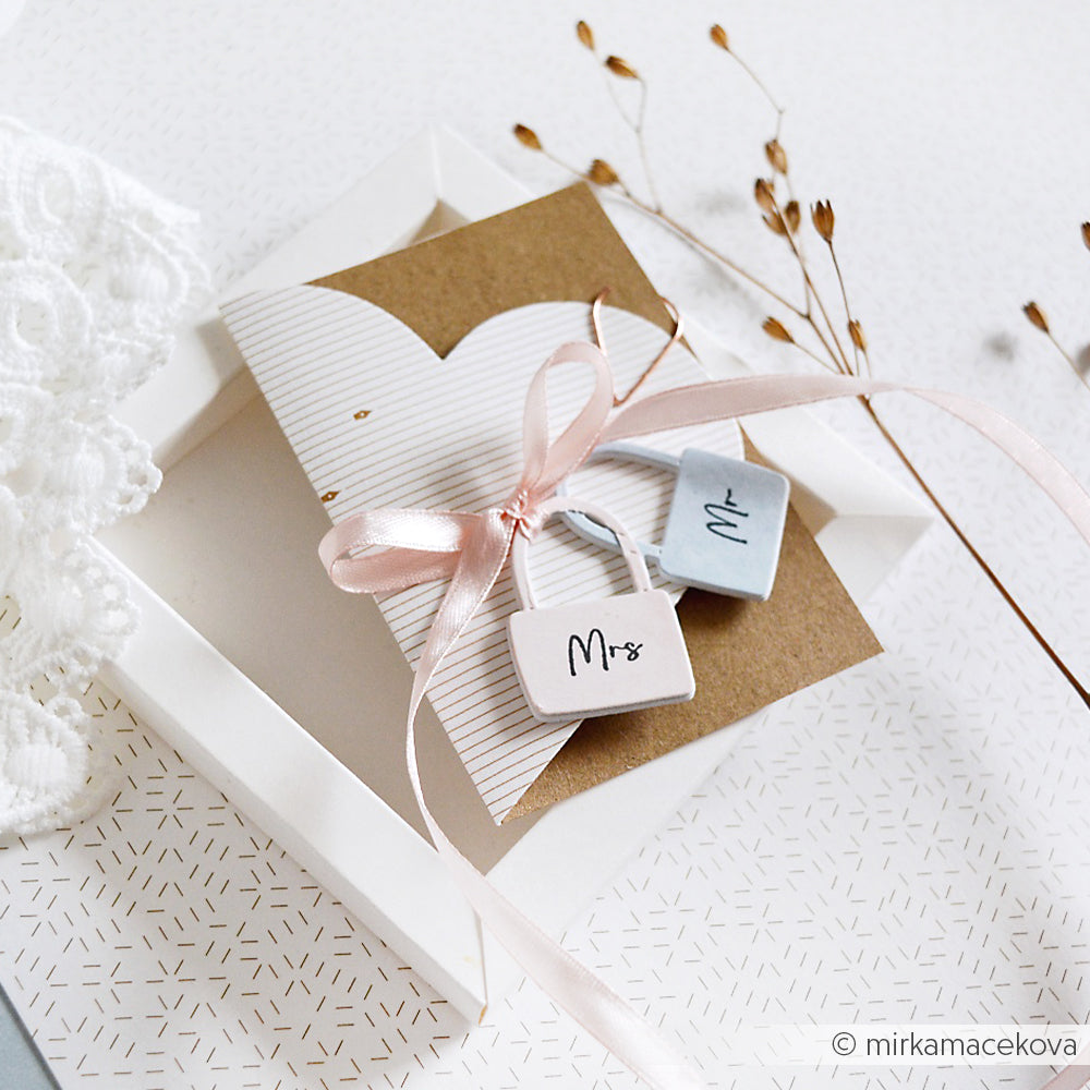 Hochzeitseinladung in einer Schachtel mit rosafarbenem Band und "Mr"- und "Mrs"-Anhängern, dekoriert mit getrockneten Blumen und veredelt mit einem eleganten Alexandra Renke-Stempel für eine einzigartige Note.