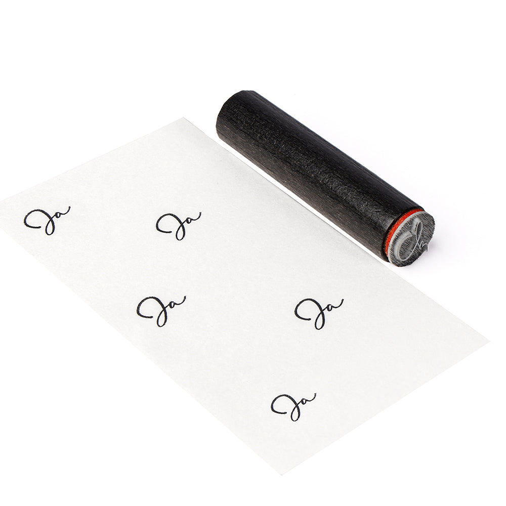 Ein schwarzer Alexandra-Renke-Gummistempel rollt wiederholt das "Ja" auf ein weißes Blatt und hinterlässt gestochen scharfe Abdrücke wie ein traditioneller Holzstempel, gepaart mit einem präzisen Stempelkissen.