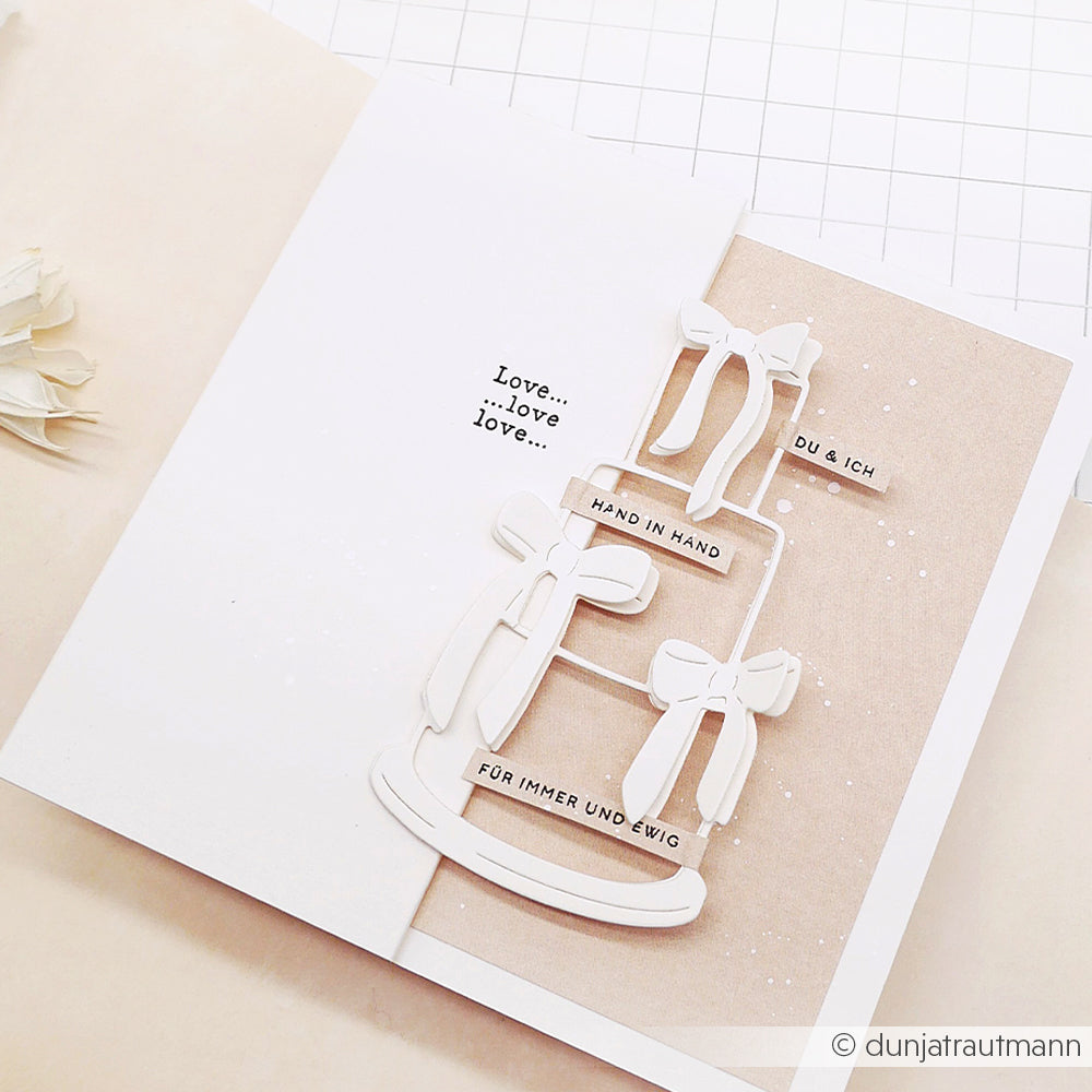 Eine handgefertigte Hochzeitskarte von Alexandra Renke mit einer weißen Torte, Schleifen und deutschen Liebessprüchen auf Beige, gestaltet mit Stempelgummi-Details und der charmanten Mini Typo Du & Ich.