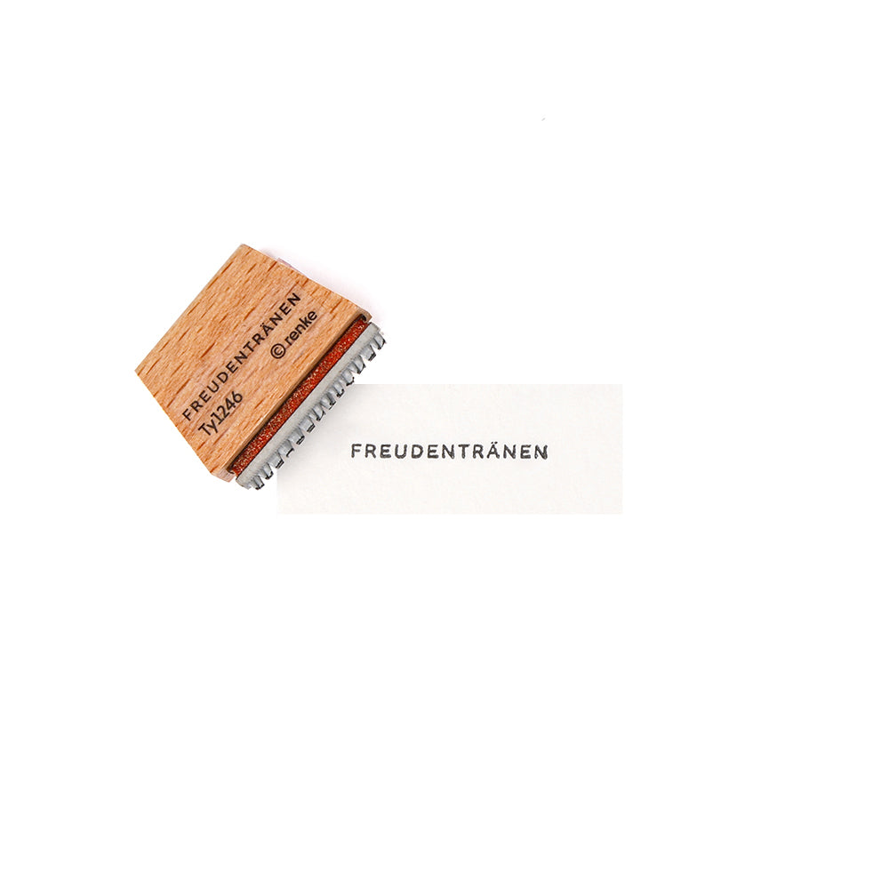 Ein Holzstempel von Alexandra Renke mit Stempelgummi und dem Aufdruck "FREUDENTRÄNEN" - ideal, um mit der Mini Typo Freudentränen einen charmanten Akzent bei Ihren Papierarbeiten zu setzen.